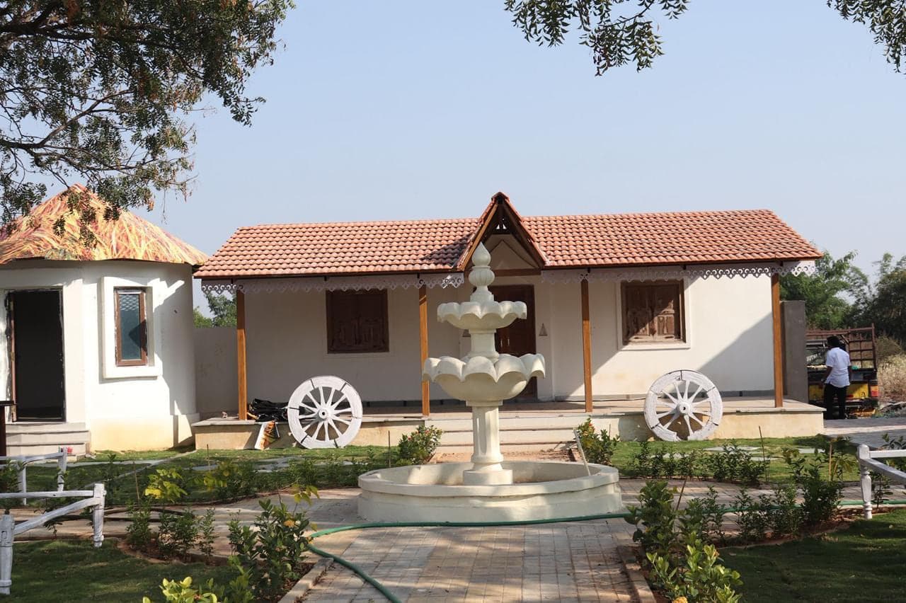 Traditional tiled-roof cottage with carved doors and painted cart wheels at Mytri Farmhouse near Kondapochamma Sagar, Siddipet