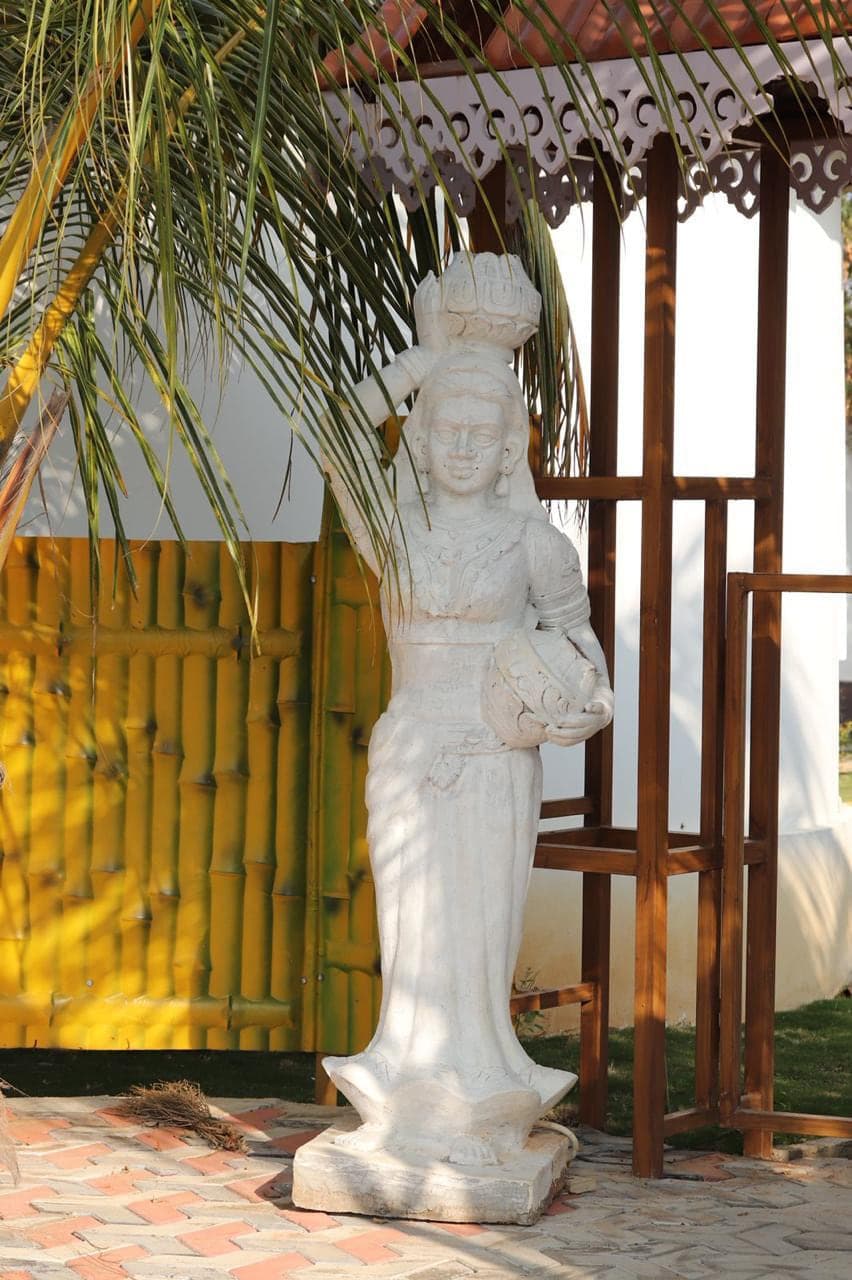 Stone statue of a woman carrying a pot, beside the bamboo screen at Mytri Farmhouse near Kondapochamma Sagar, Siddipet