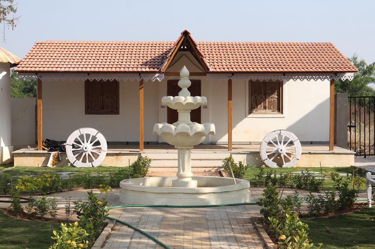 Fountain on the lawn in front of a traditional cottage at Mytri Farmhouse near Kondapochamma Sagar, Siddipet
