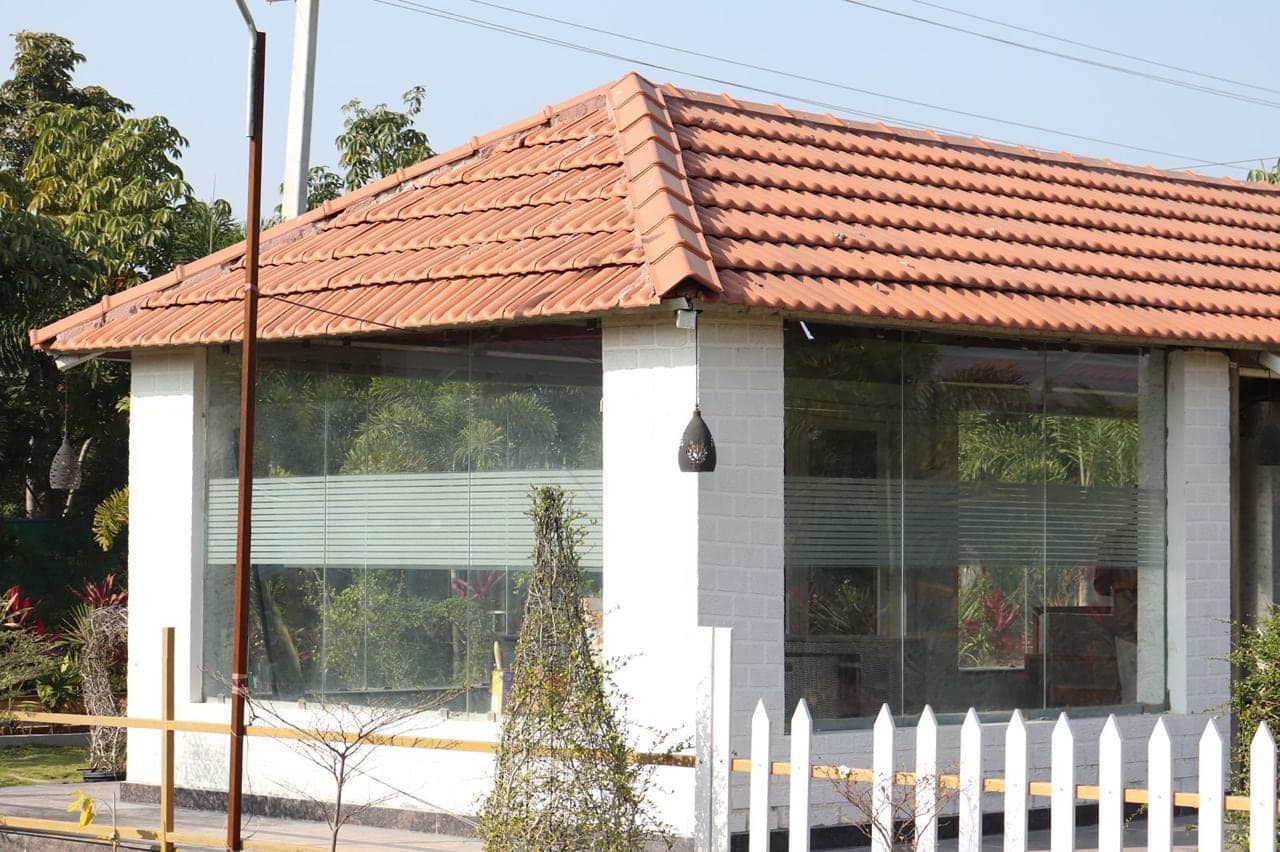 Glass-fronted dining pavilion seen across the lawn at Mytri Farmhouse near Kondapochamma Sagar, Siddipet