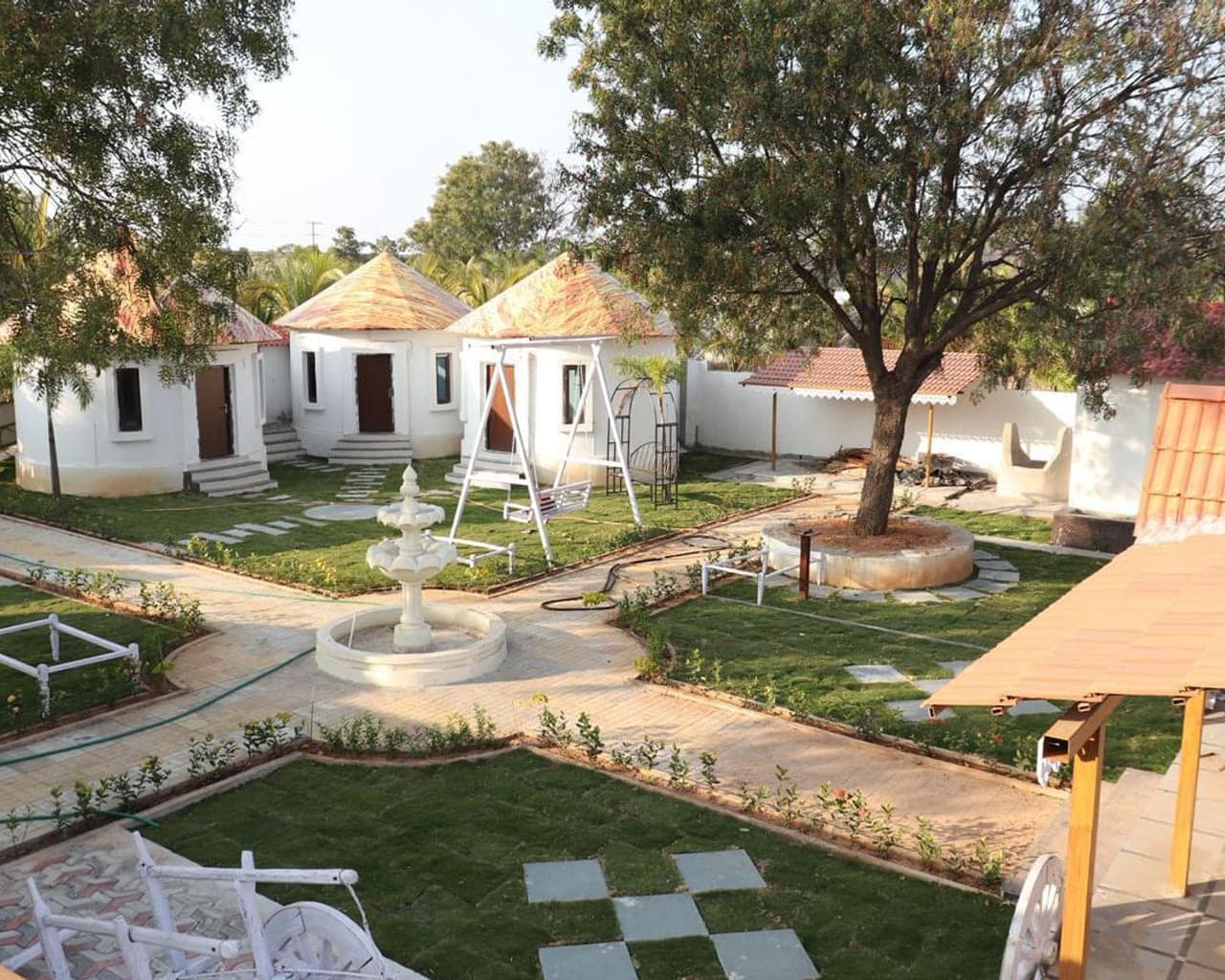 Round guest cottages, a garden swing and a stone fountain in the central courtyard at Mytri Farmhouse near Kondapochamma Sagar, Siddipet