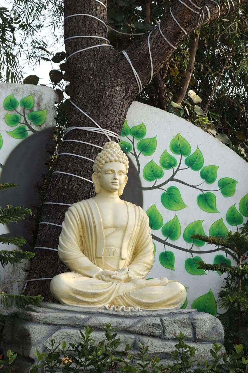 Seated Buddha statue against a painted peepal-leaf wall at Mytri Farmhouse near Kondapochamma Sagar, Siddipet