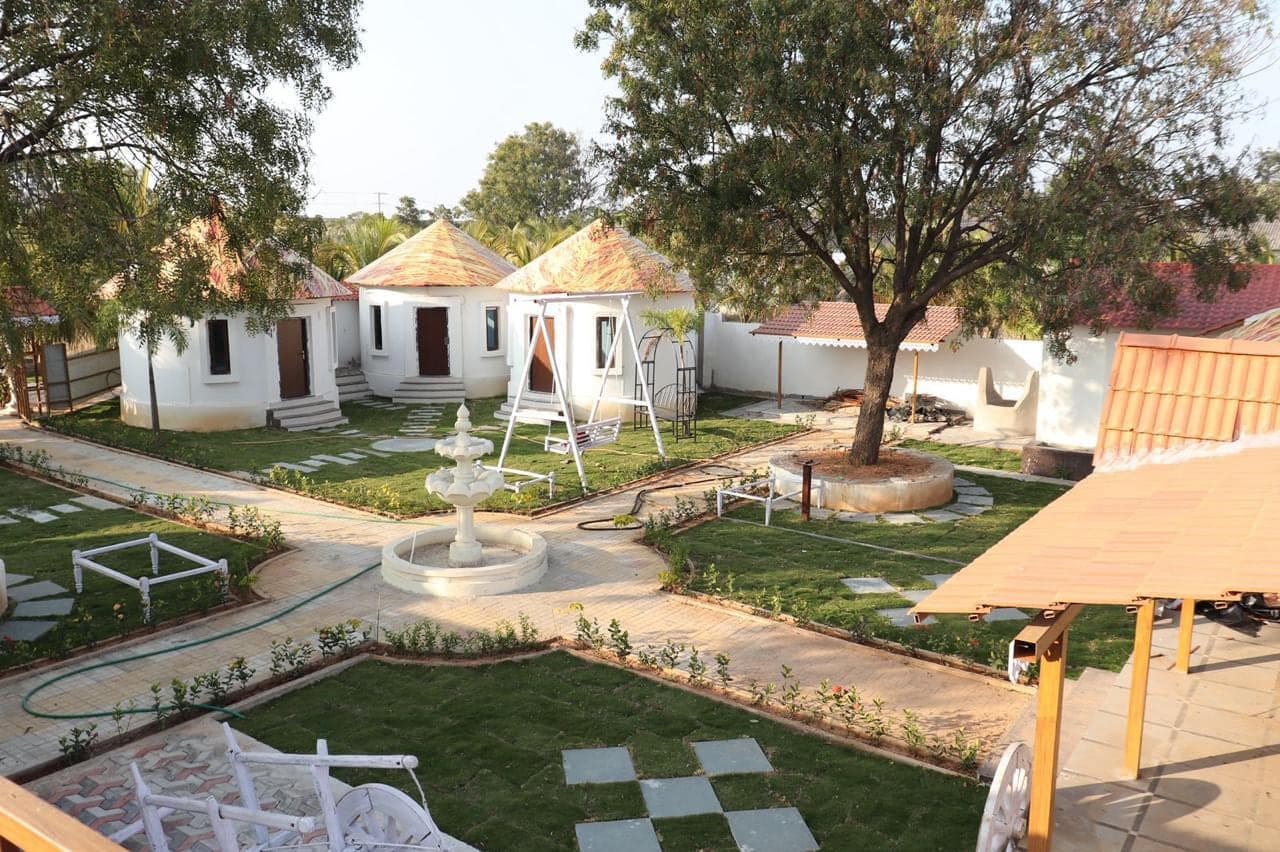 Round guest cottages, a garden swing and a stone fountain in the courtyard at Mytri Farmhouse near Kondapochamma Sagar, Siddipet